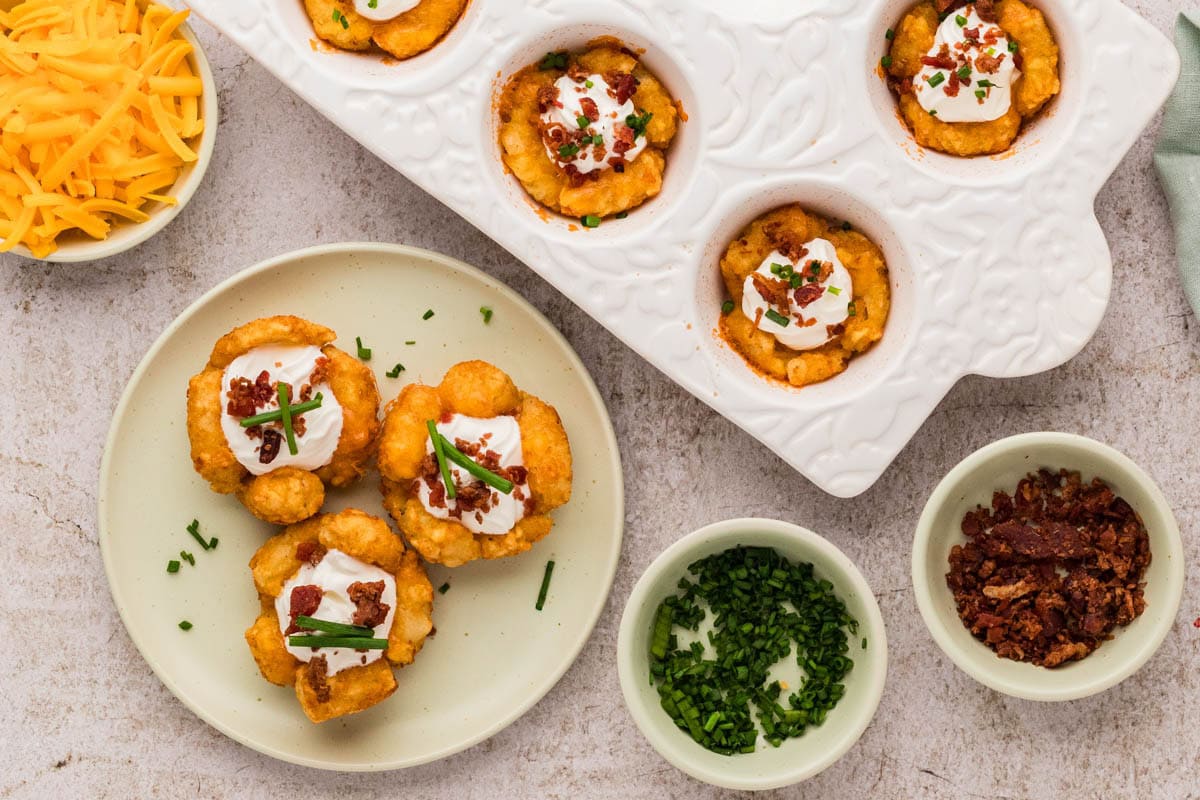 Loaded tater tot cups served on a plate next to more in a muffin dish.