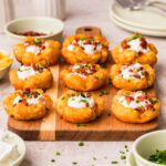 Side view of loaded tater tot cups lined up on a wooden board.