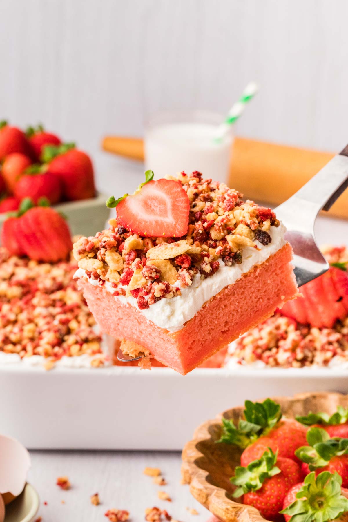 Slice of strawberry crunch cake on a metal spatula with more cake behind it.