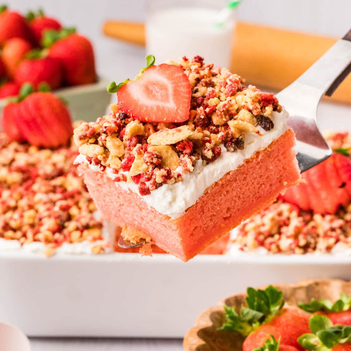 Slice of strawberry crunch cake on a metal spatula with a fresh strawberry on top.
