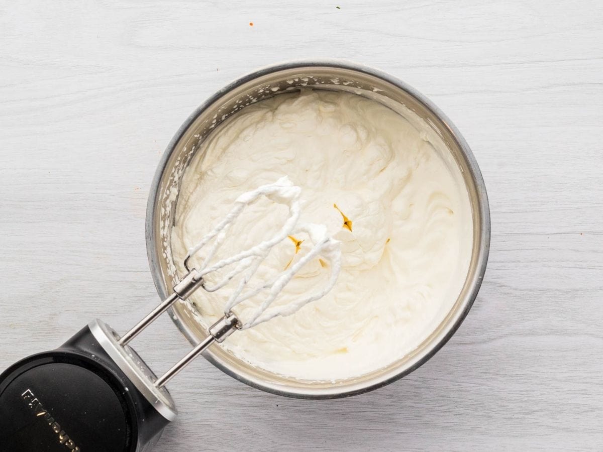 Whipped cream icing whipped together in a mixing bowl with a hand mixer.