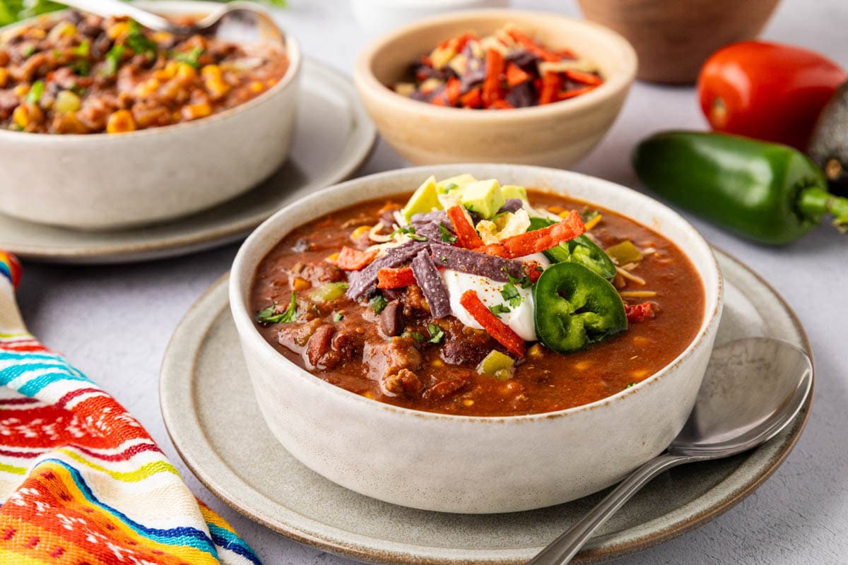 A bowl of taco soup with ground beef and all the fixings on top,