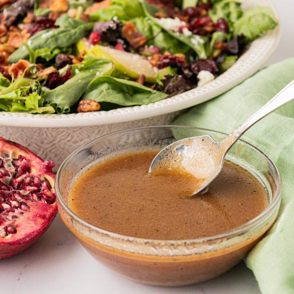 A bowl with apple vinaigrette with a salad in the background.