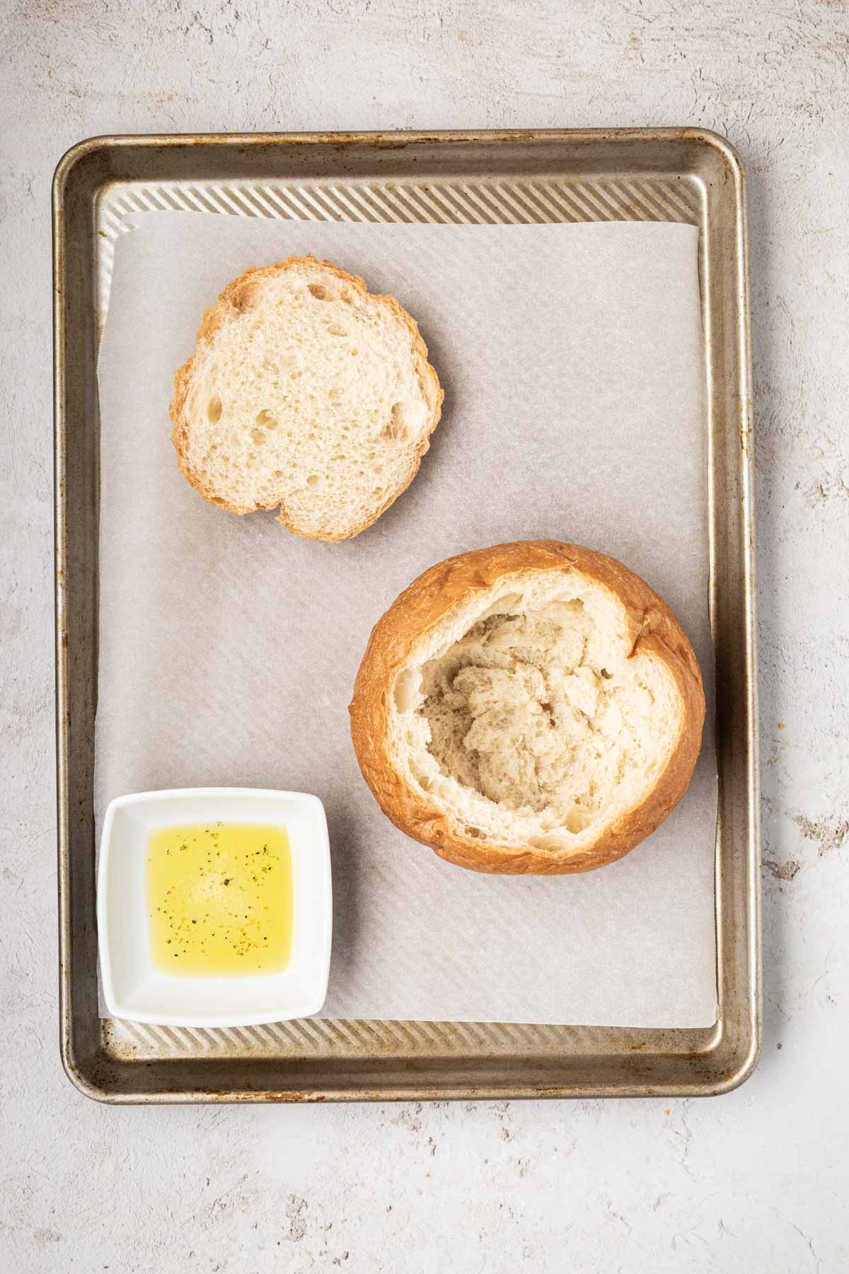 Bread hollowed out on a sheet pan next to a small bowl of melted butter.