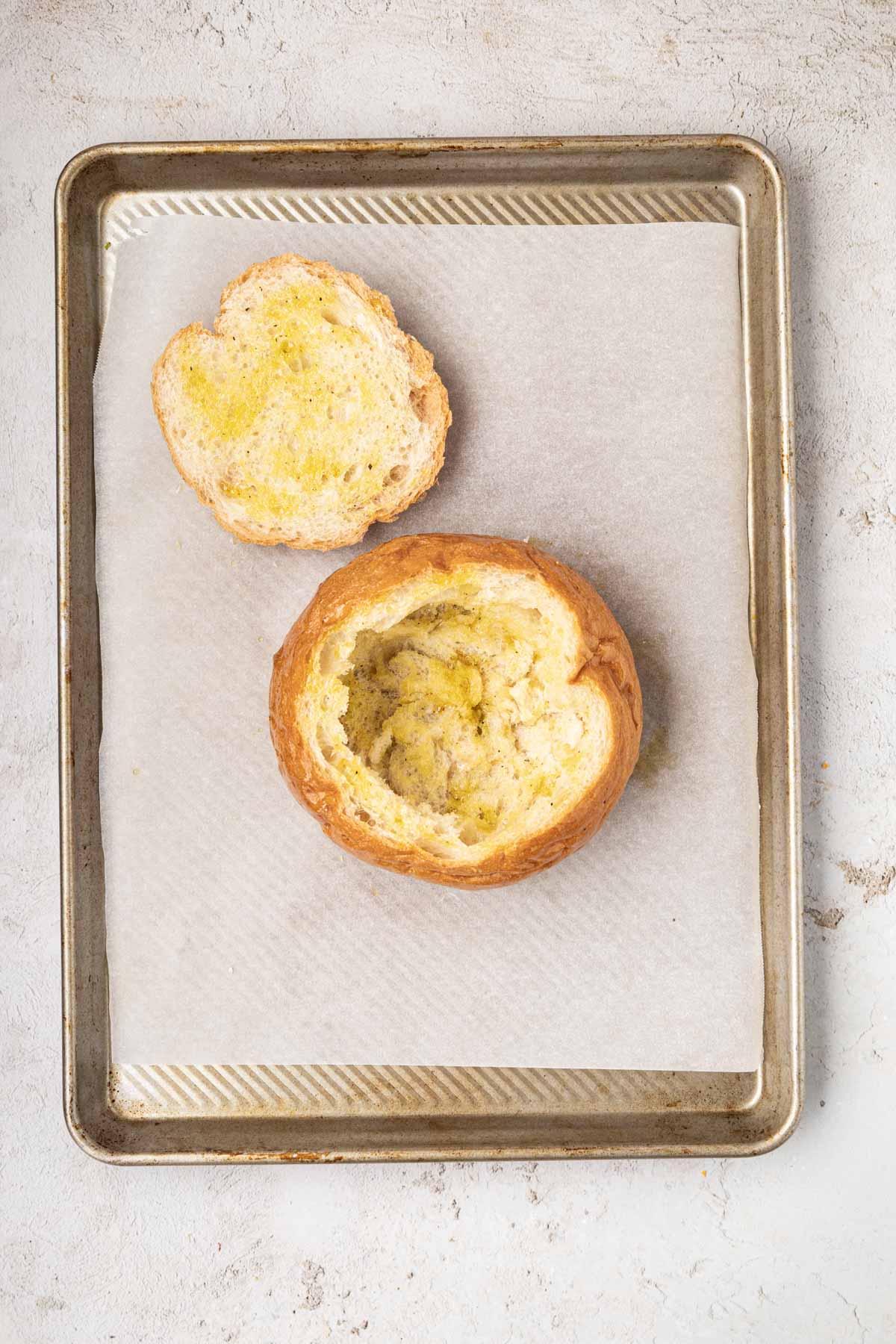 Bread bowl with melted butter on it on a sheet pan.