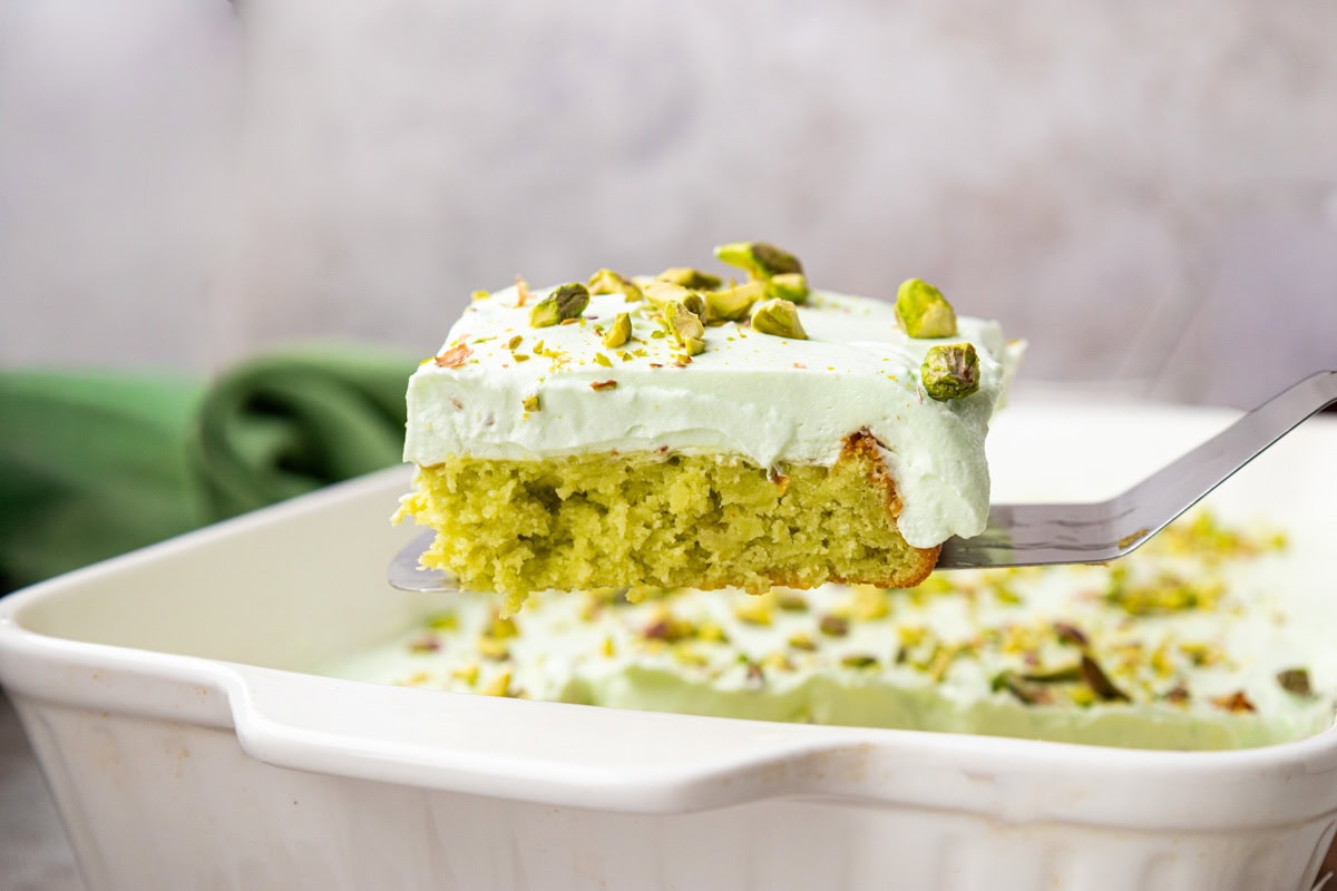 Side view of a slice of pistachio pineapple cake on a metal spatula.