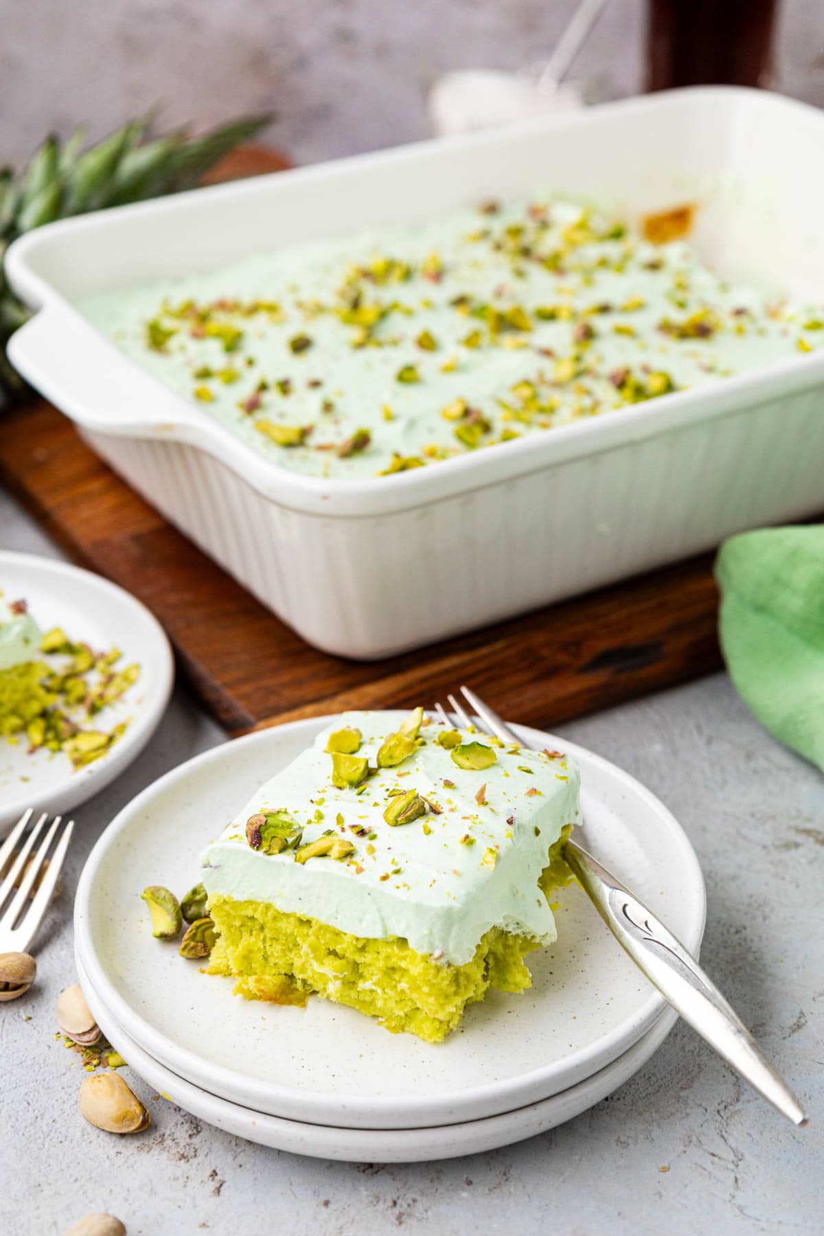 Slice of pistachio pineapple cake on a plate with more cake in the dish in the background.