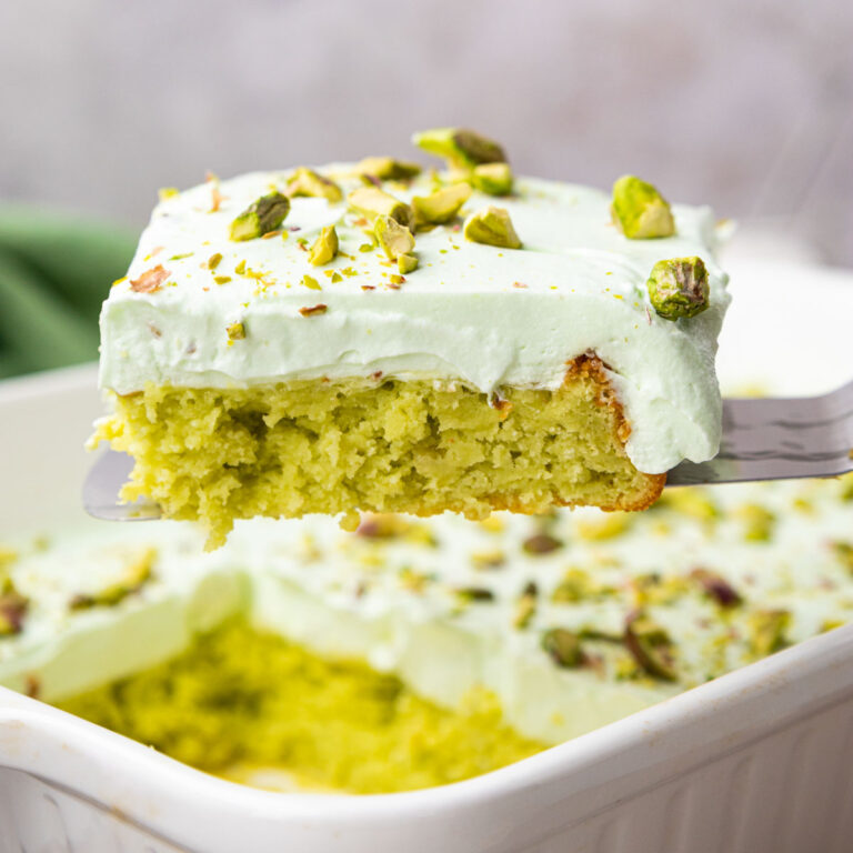 Side of pistachio pineapple cake on a metal spatula hovering over the rest of the cake.