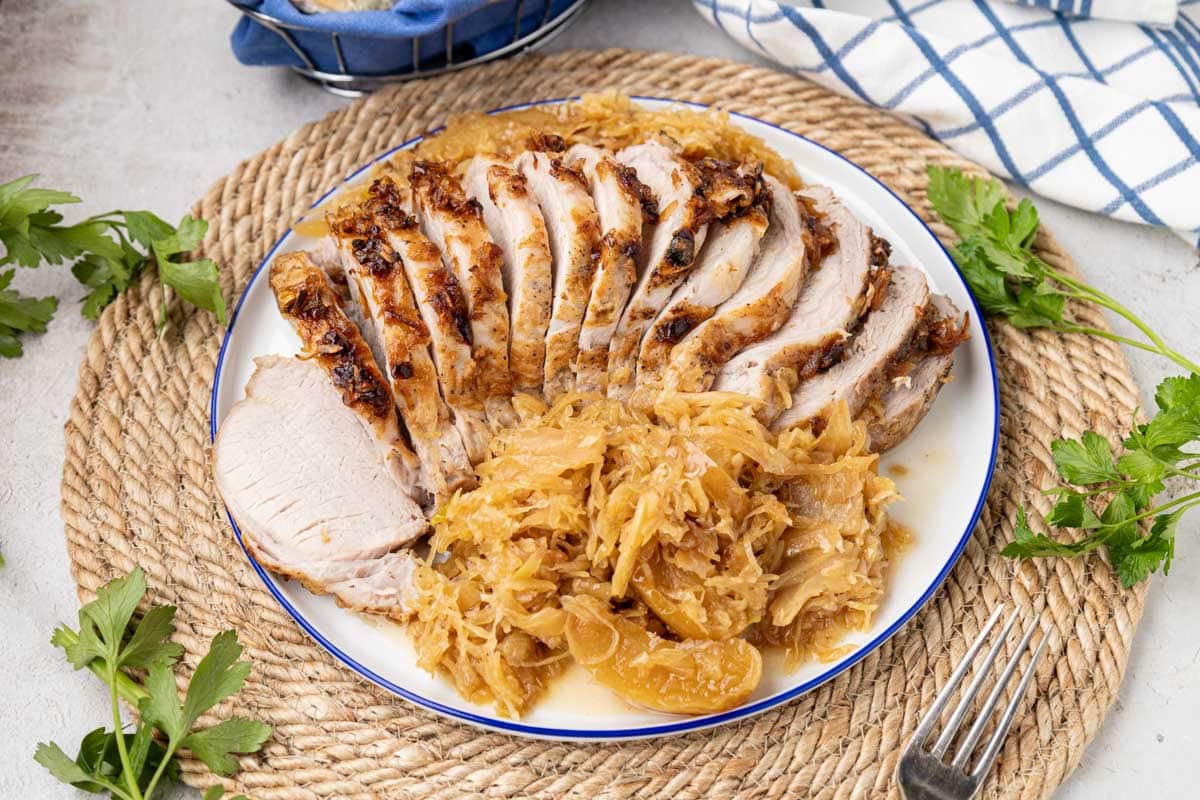 Sliced pork roast with sauerkraut and apples on a serving platter.