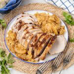 Sliced pork roast with sauerkraut and apples on a serving platter.
