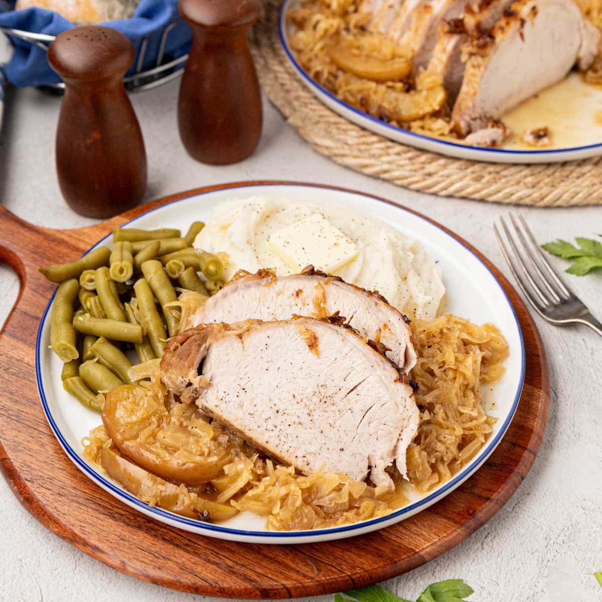 Pork Roast with sauerkraut on a white plate with green beans.