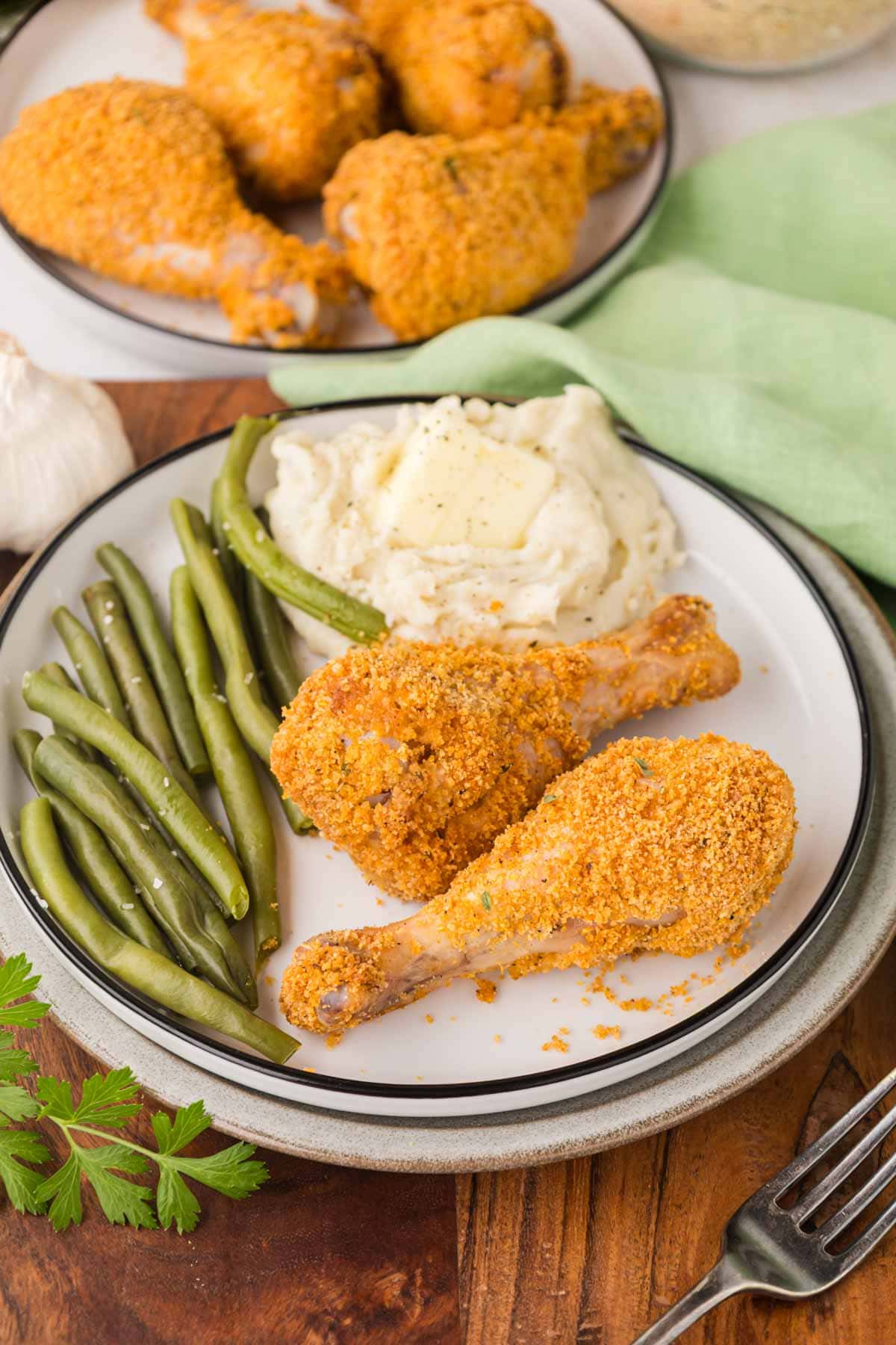 To shake and bake chicken drumsticks on a plate with mashed potatoes and green beans.
