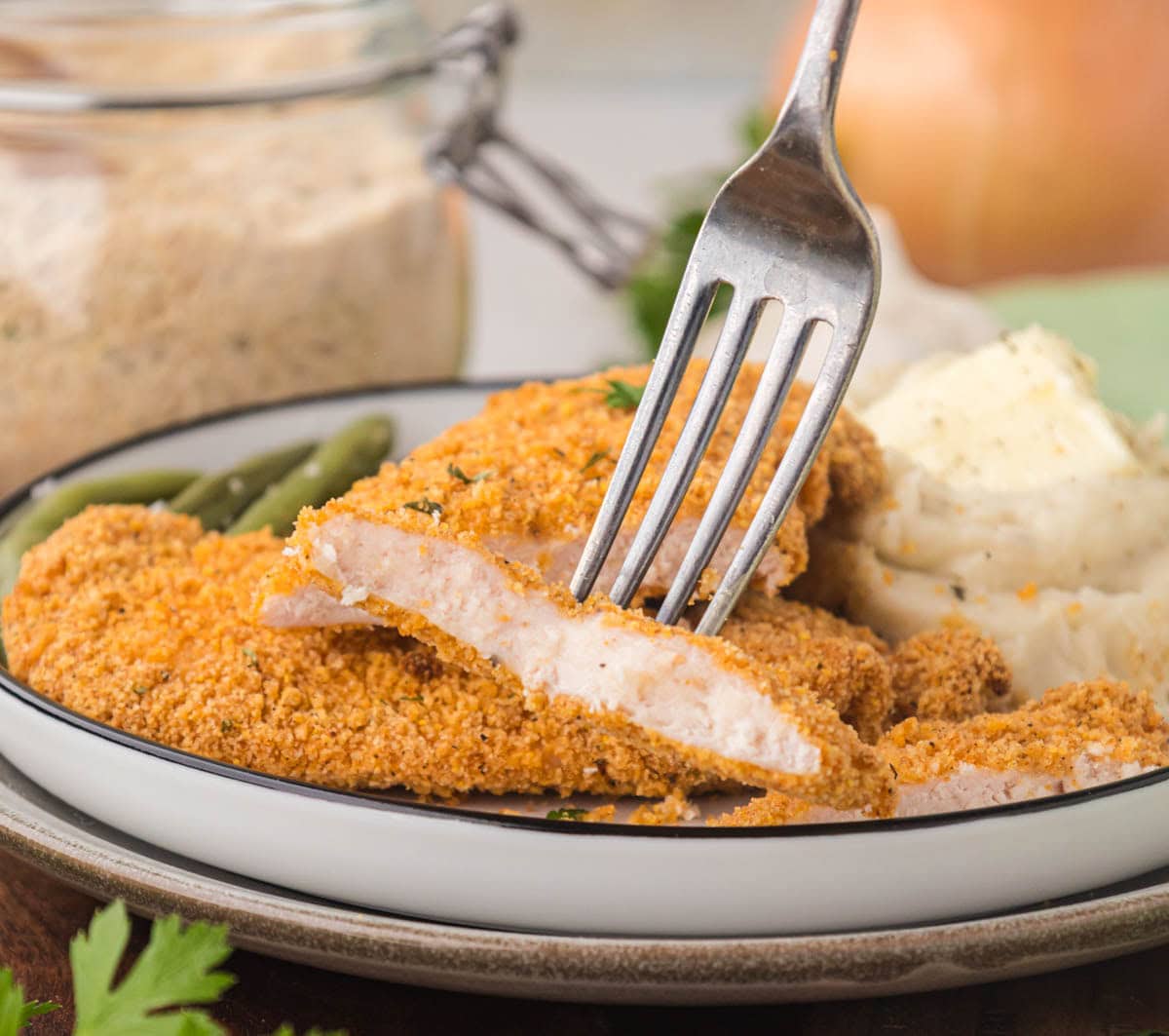 A fork, removing a bite of shake and bake chicken cutlet.