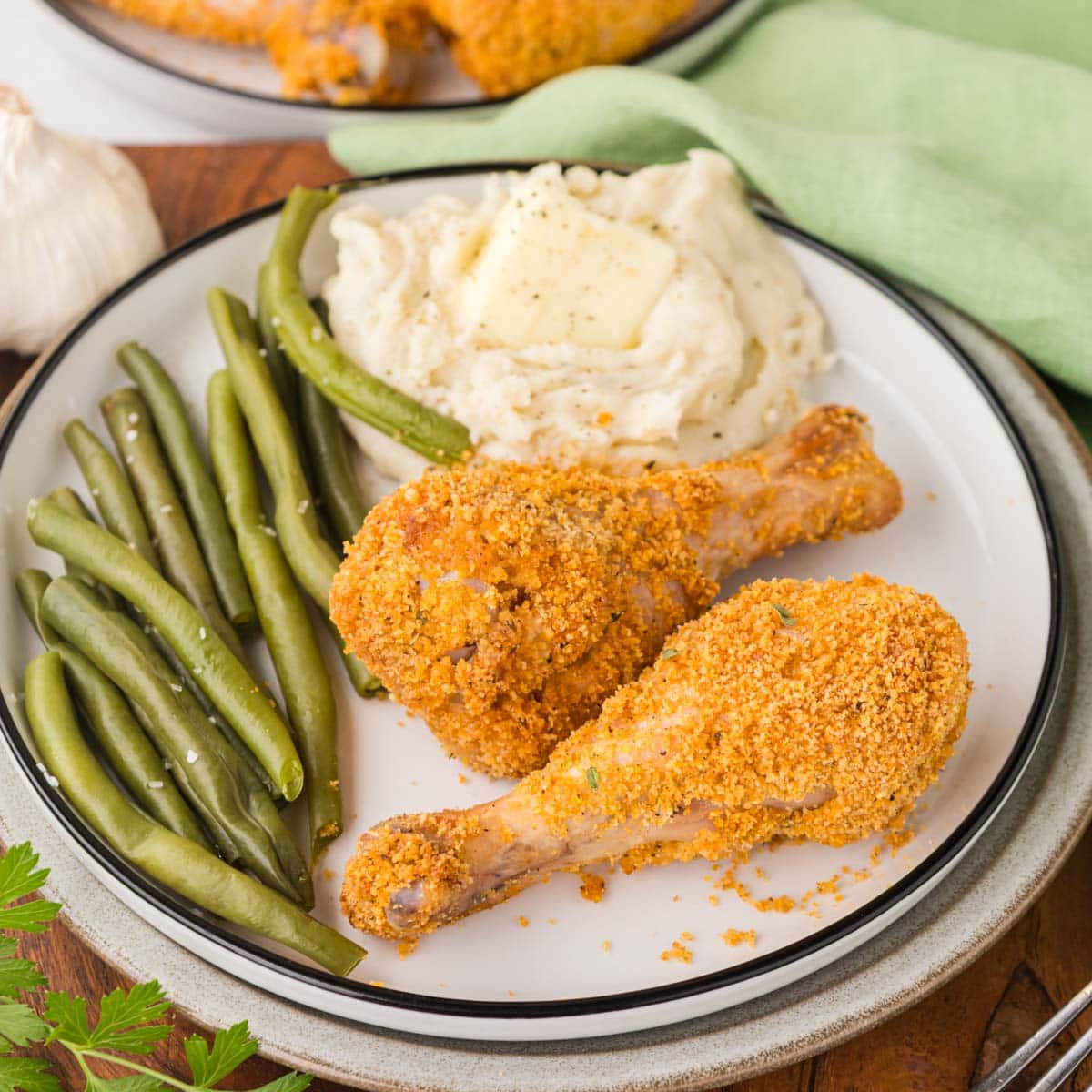 Shake and bake chicken drumsticks on a plate with mashed potatoes and green beans.