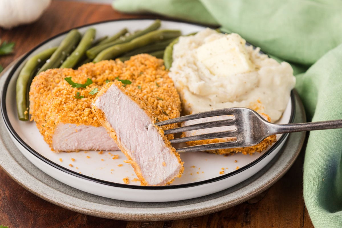 Shake and bake pork chop on a plate with mashed potatoes and green beans.