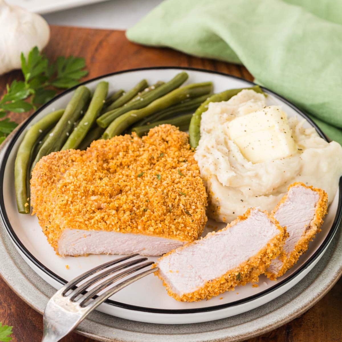 Shake and bake pork chop on a plate with mashed potatoes and green beans.