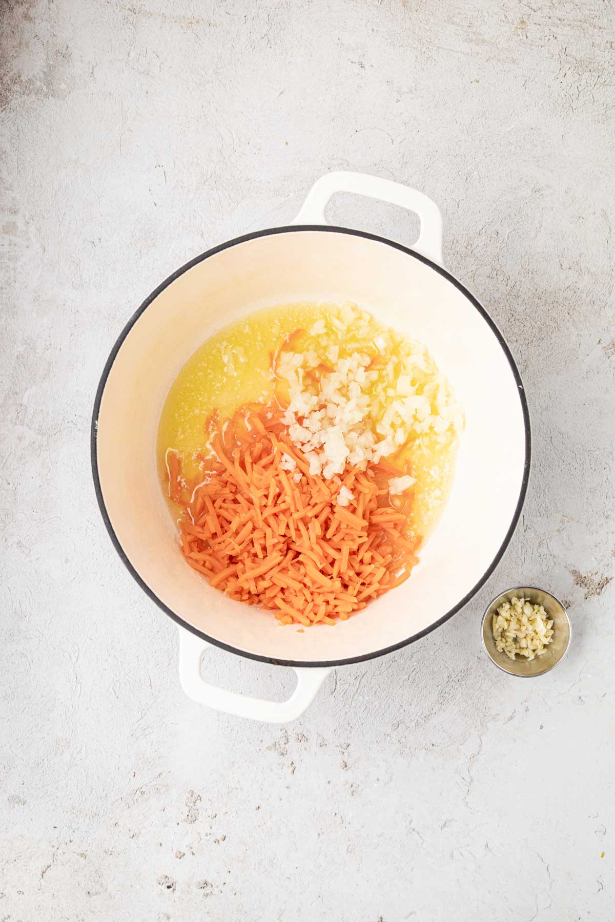 Onion and carrots added to a pot with melted butter.