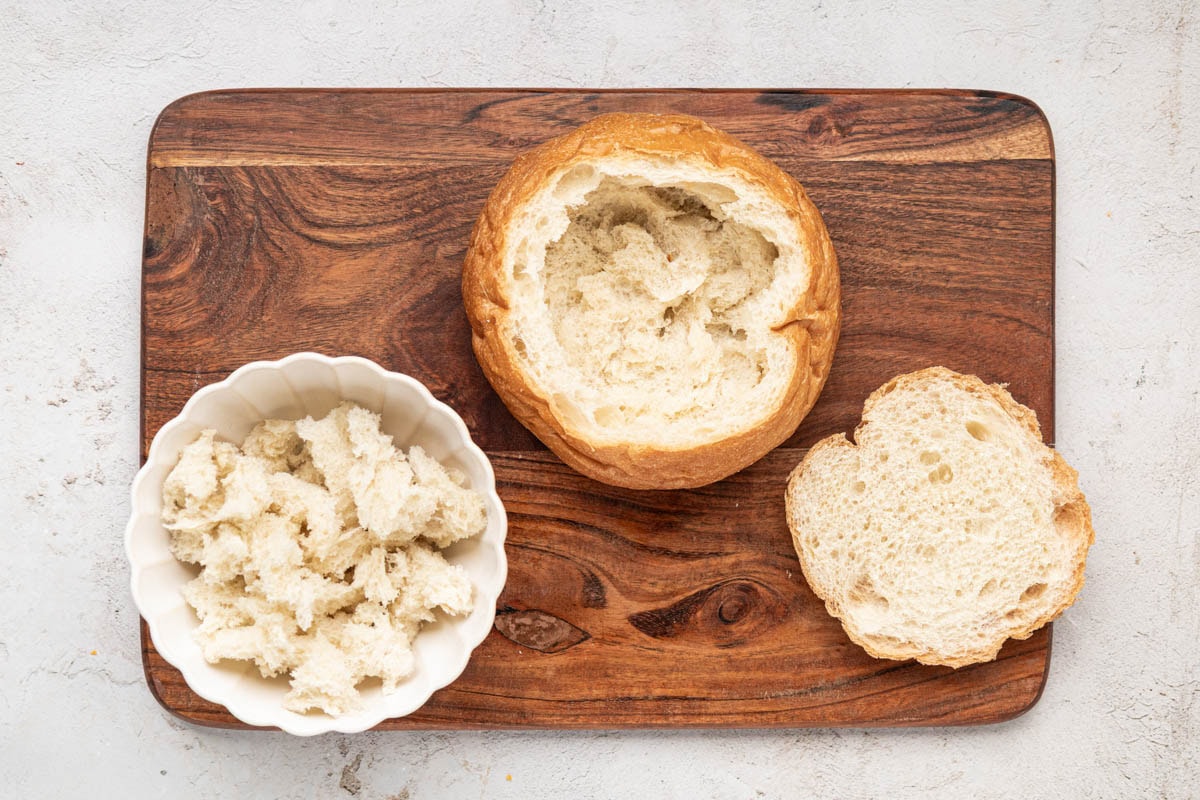 A bread bowl with top cut off and inside hollowed out and pulled apart into pieces.