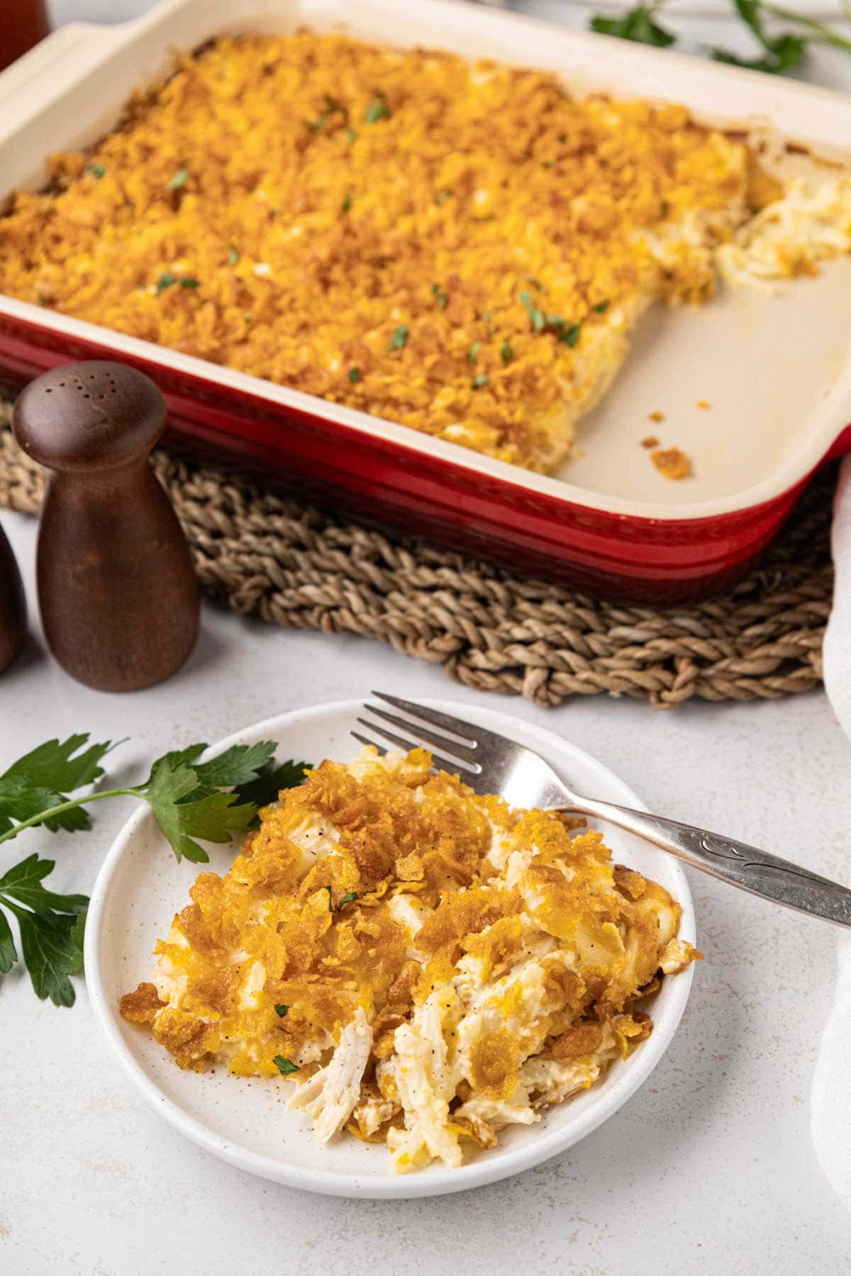 Chicken hash brown casserole served on a plate with the rest of the casserole in the background.