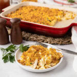 Chicken hash brown casserole served on a plate with more casserole in the backgrouhd.