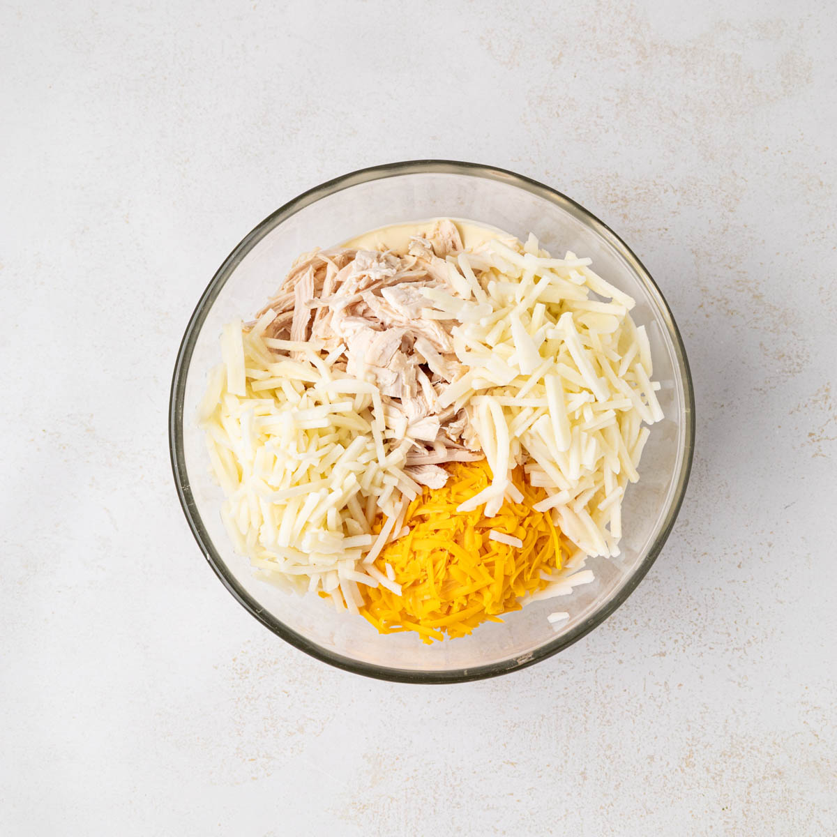 Chicken, hash browns and cheese added to the sauce mixture in a bowl.