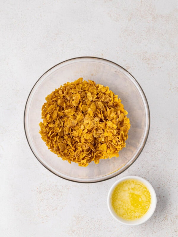 Cornflakes in a bowl next to some melted butter.