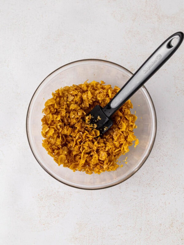Cornflakes mixed with melted butter in a bowl.