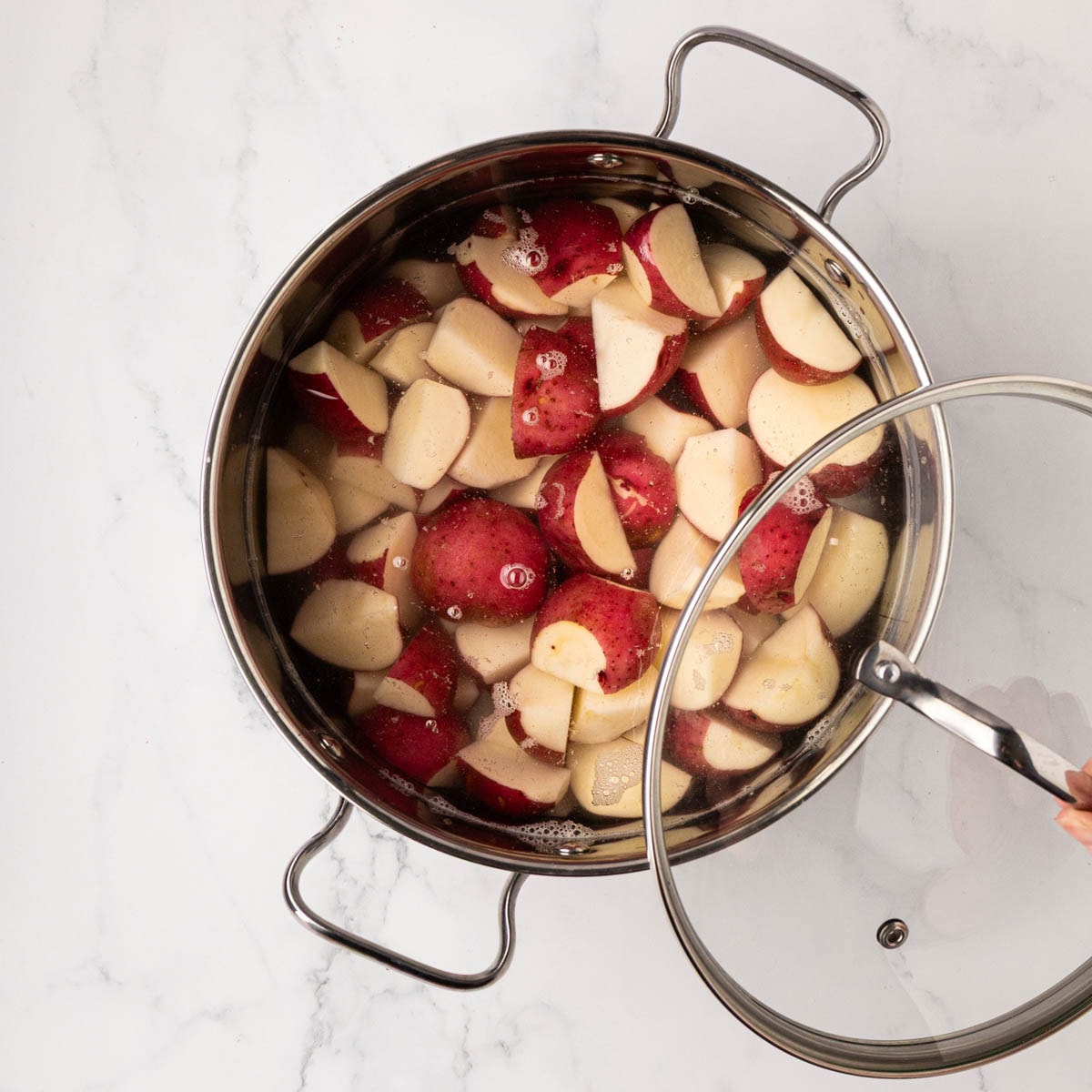 Red potatoes, cut, and quartered in a pot.