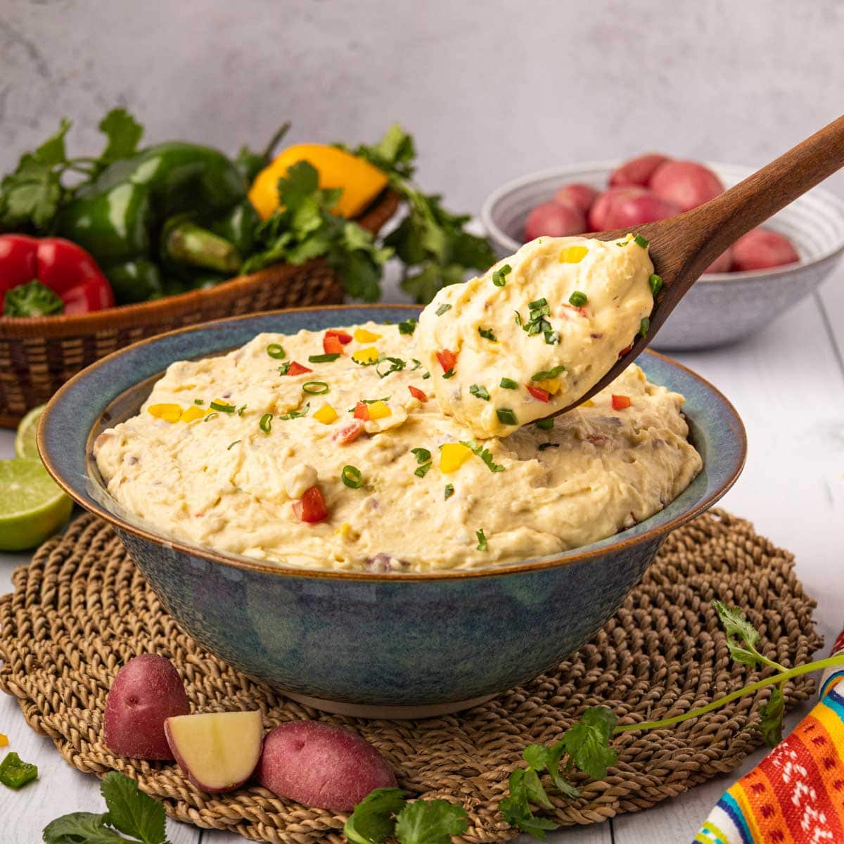 A wooden spoon removing a serving Mexican mashed potatoes from a blue bowl.