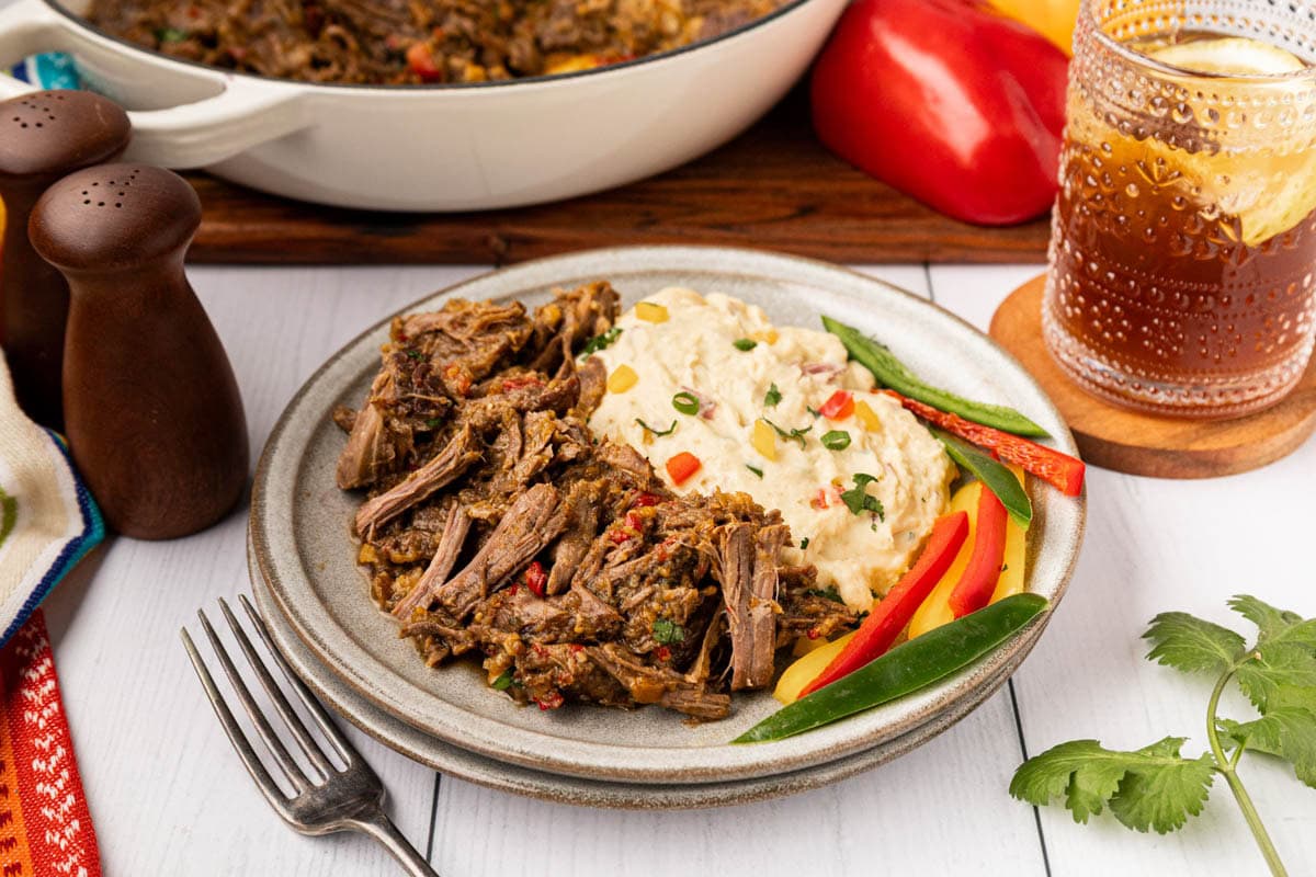 Mexican pot roast on a plate with papas con chiles and sliced bell peppers.