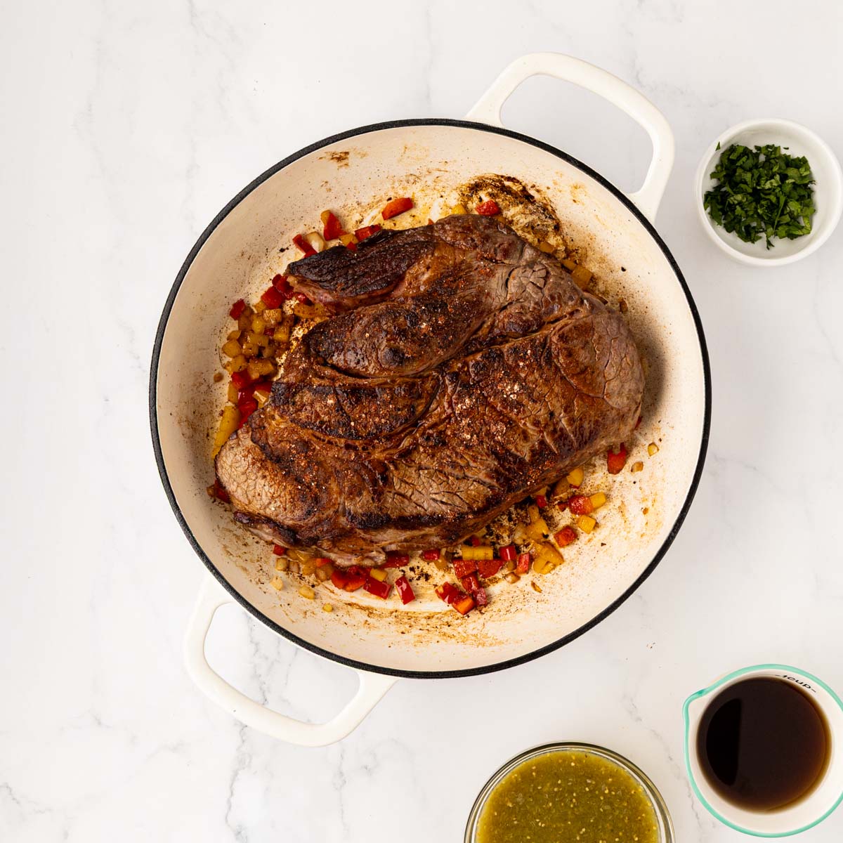Adding the seared pot roast back to the sauteed veggies in a Dutch oven.