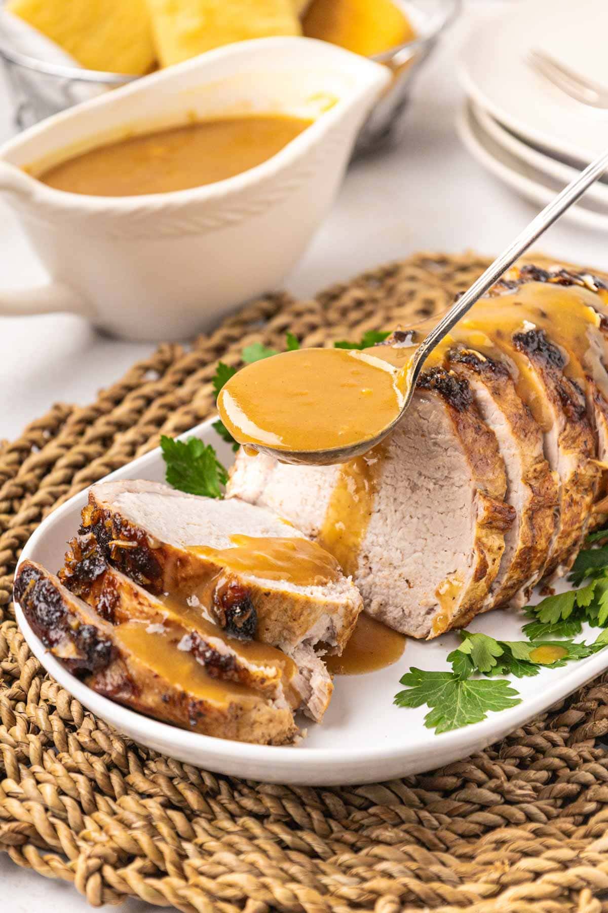 Pouring pork gravy over a sliced pork roast on a plate.