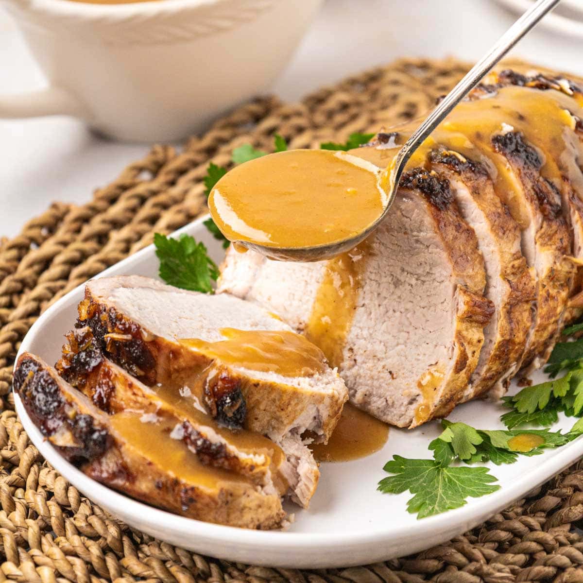Metal ladle pouring pork gravy on top of a pork roast on a serving platter.