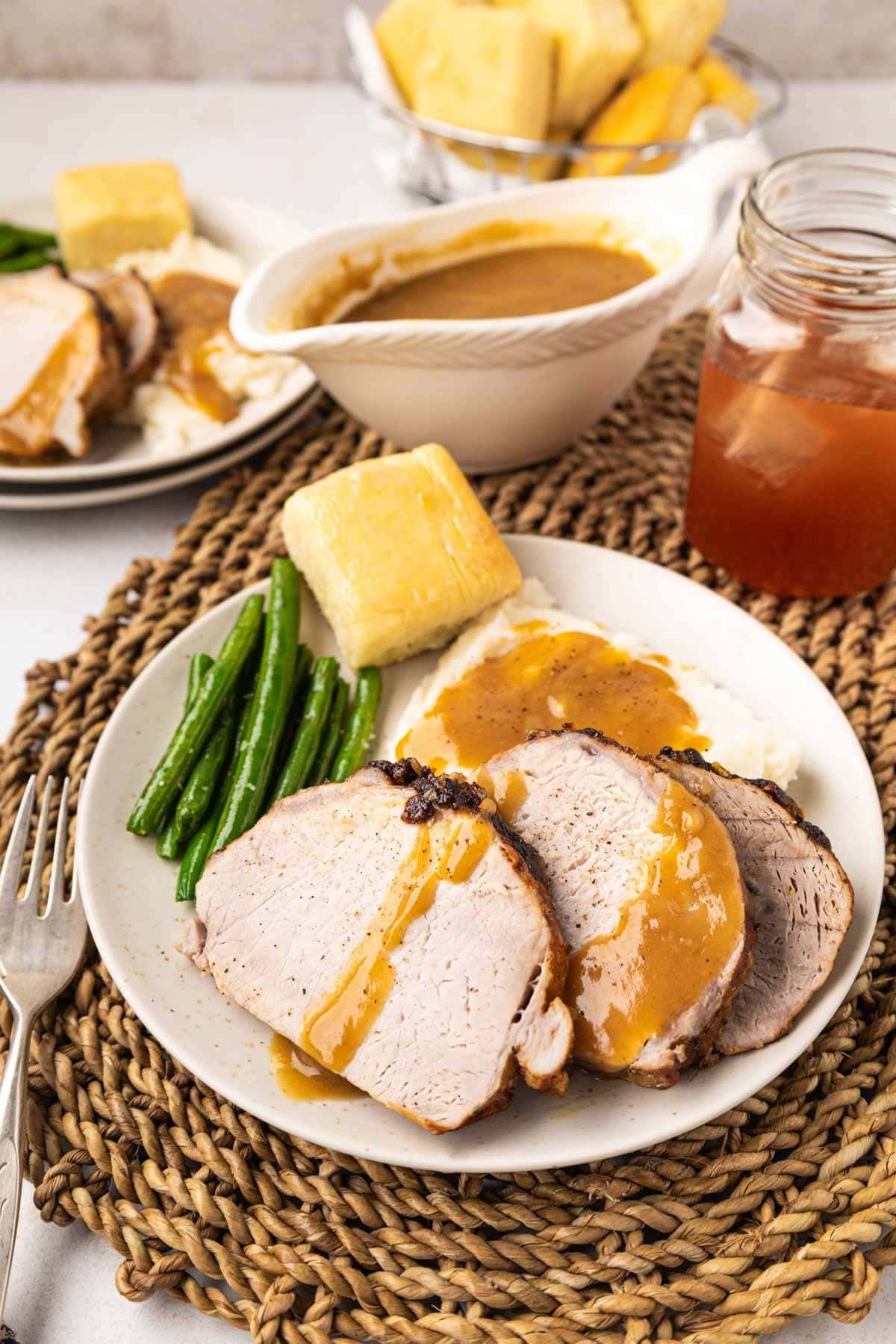 Slices of roasted pork oin on a plat with mashed potatoes, a roll and green beans.