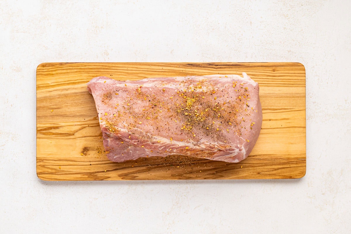 Pork roast being seasoned on a wooden board.