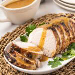 Close up of a sliced oven baked pork roast on a serving platter with gravy on top.