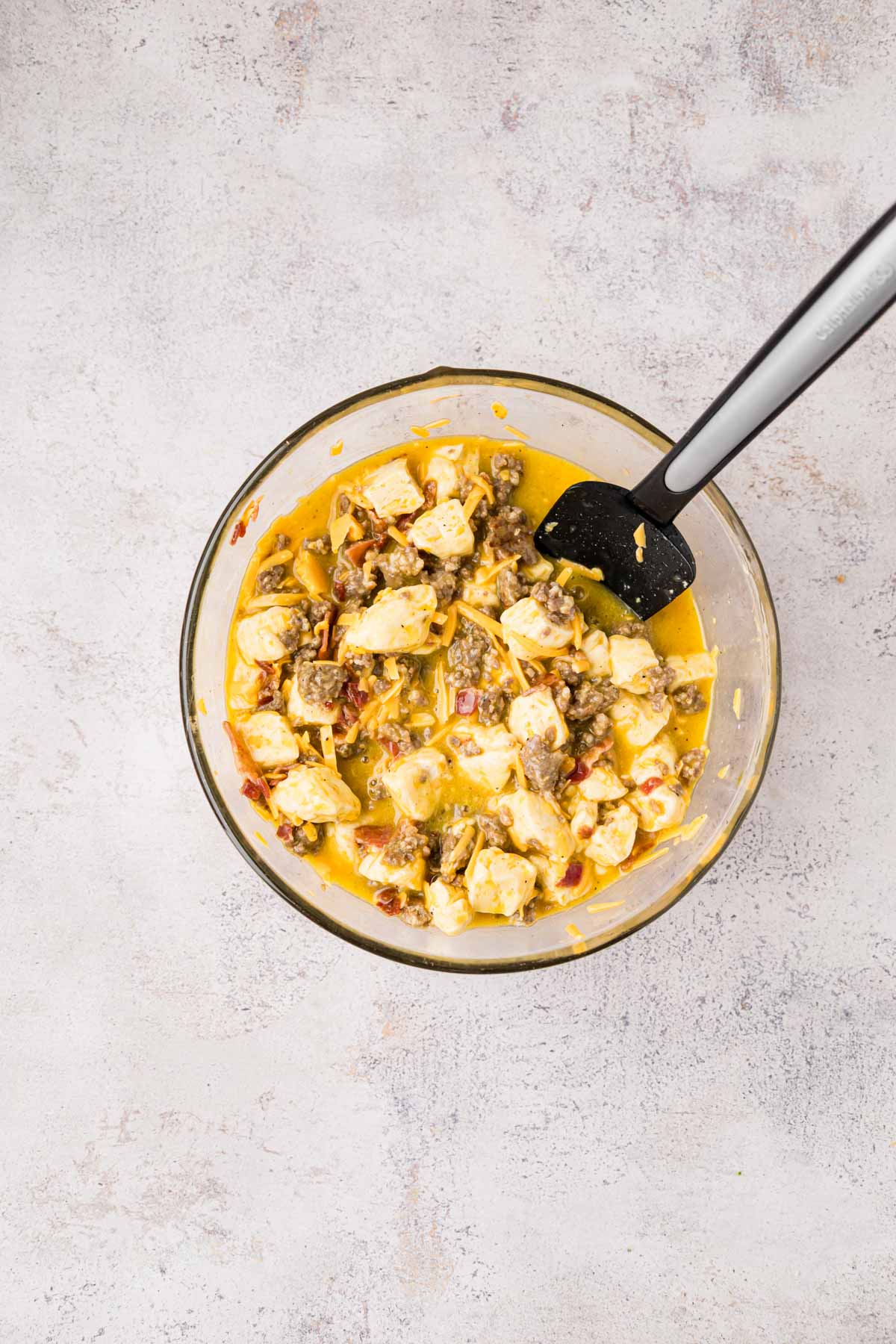 Folding together the biscuits, meats, cheese and eggs in a bowl.