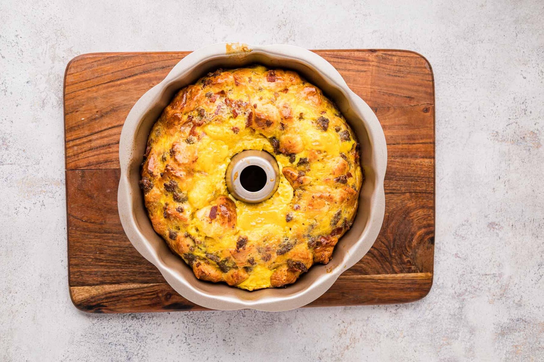 Baked breakfast casserole with biscuits in a bundt pan on a wooden board.