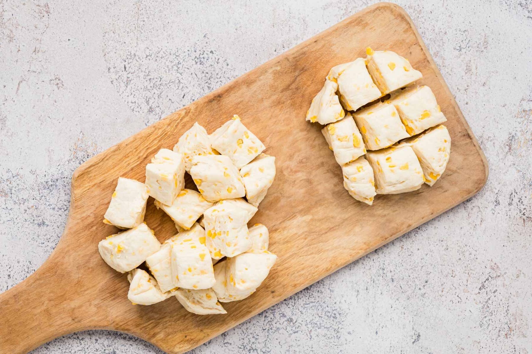 Slicing canned biscuits into small squares on a wooden board.