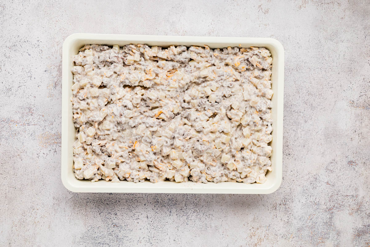 Hamburger hash brown mixture placed into a white baking dish before baking.