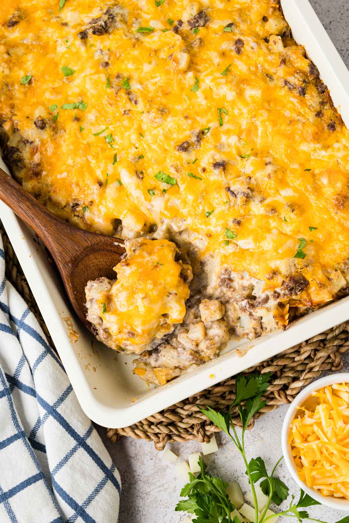 Hamburger hash brown casserole in a white baking dish with a wooden spoon scooping some up.