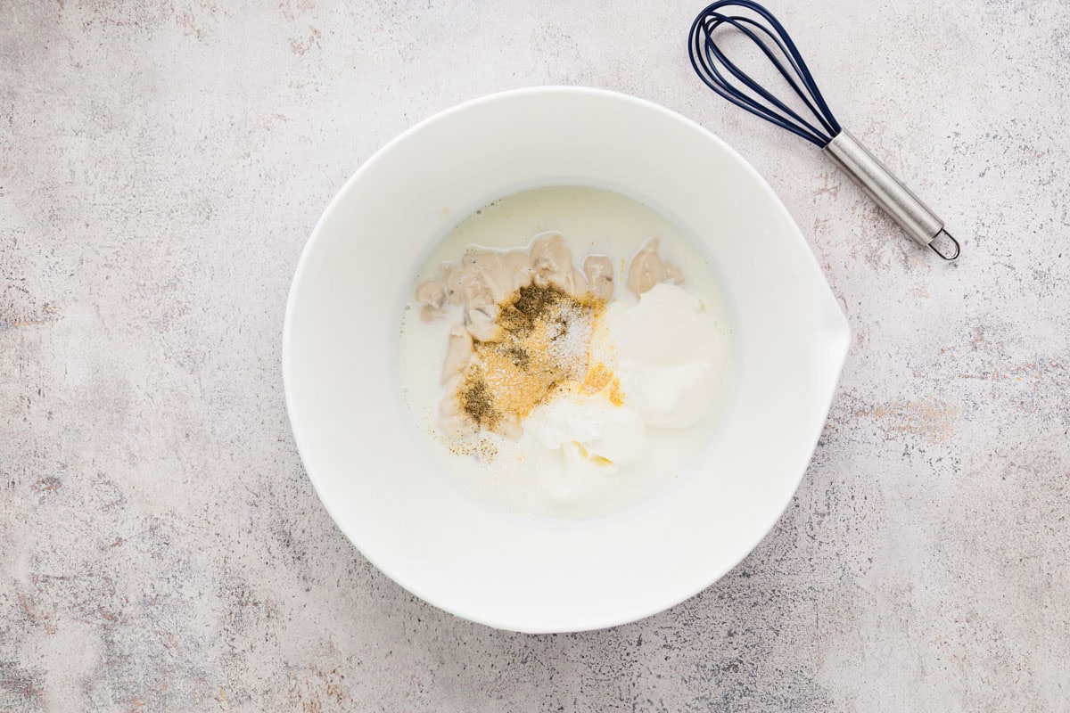 Cream of mushroom soup, sour cream, milk, and spices in a bowl before being whisked.