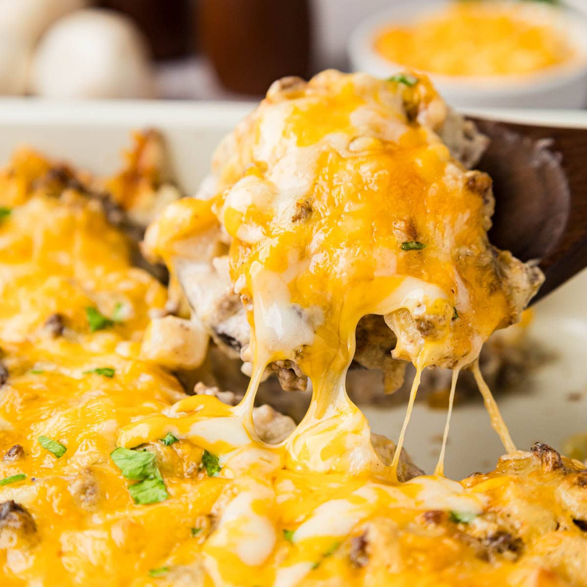 Wooden spoon scooping up a portion of hamburger hash brown casserole from a baking dish.