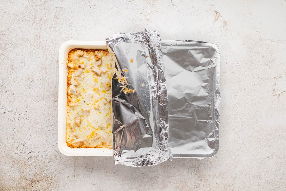 Taking off the foil on the casserole to allow it to bake uncovered.