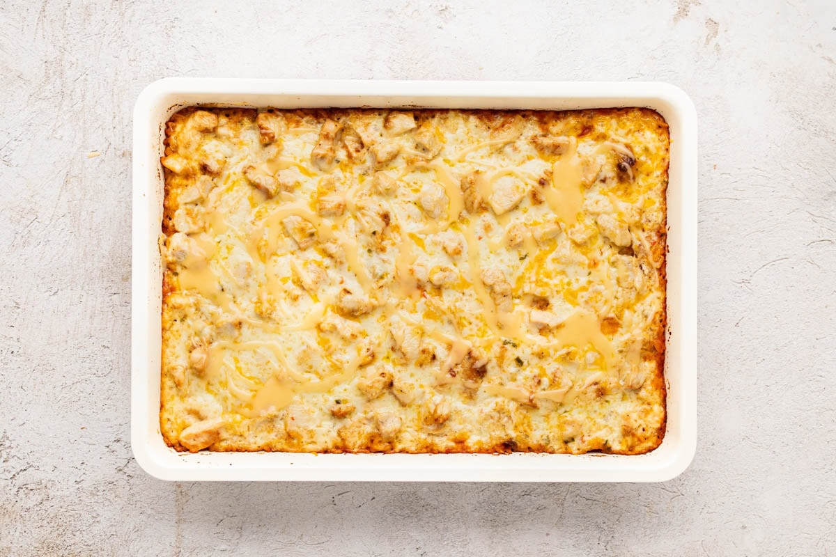 Finished queso, chicken and rice casserole in a white baking dish with queso on top.