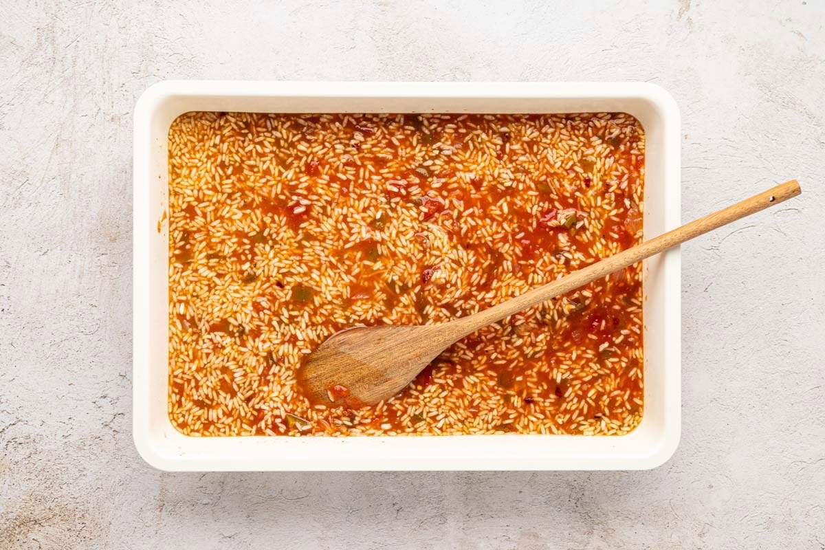 Rice, broth, water, and salsa mixed together in a white baking dish.