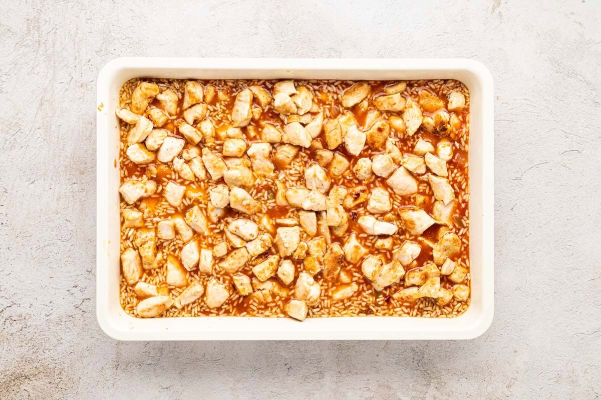Chicken added to the rice mixture in a white baking dish.
