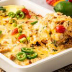 Scooping a portion of queso chicken and rice casserole from a baking dish.
