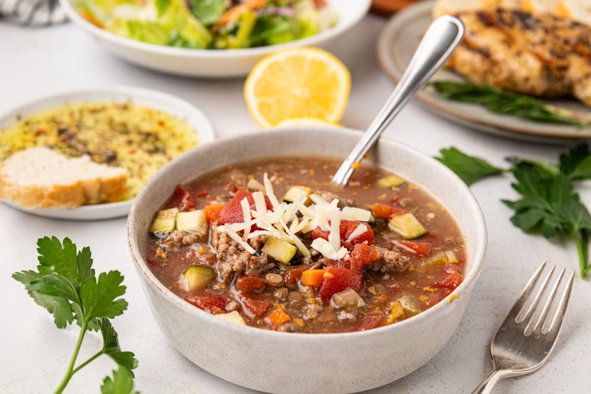 A bowl of lentil soup with talian bread in the background.