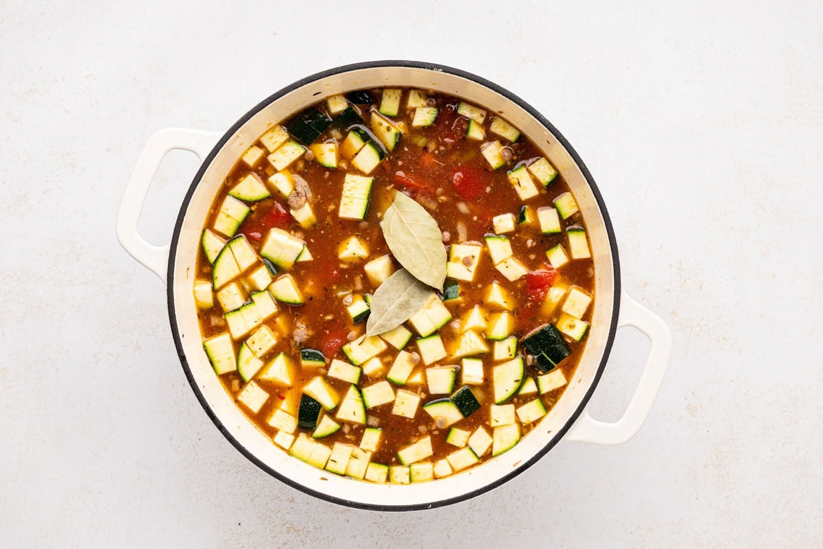 Broth stirred into the pot and bay leaves added to the top before simmering.